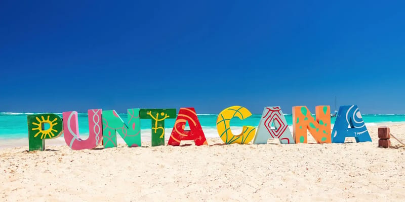 Colorful Punta Cana sign on a sandy beach with the ocean behind it.